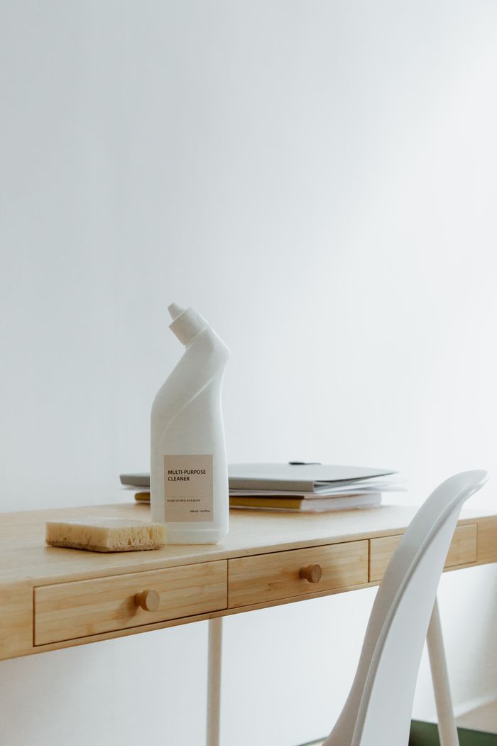 A tidy, well-arranged home office desk with a cleaner bottle and sponge, highlighting simplicity and practicality.
